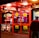 A brightly lit entrance to a casino with neon signs, including one advertising a £500 jackpot. The doors have clear signage indicating entry is restricted to those over 18. A person in a red jacket stands to the right, possibly interacting with a machine or display.
